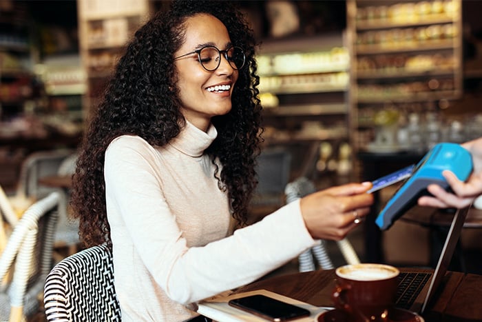 happy woman with glasses pays for coffee with her debit card using merchant services