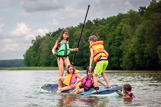 Group of children laughing and having fun with a stand-up paddle board on Lake Carlos near Alex