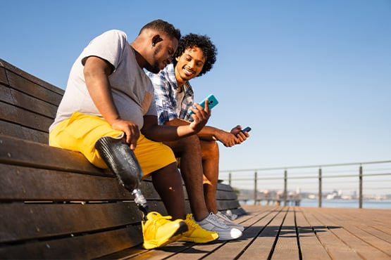 two happy male friends sit together and use phone to move money