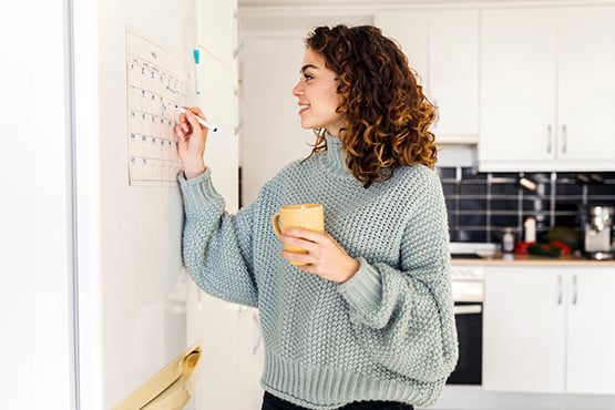 Curly-haired woman in sage sweater circles the closing date for her new home on a whiteboard calendar