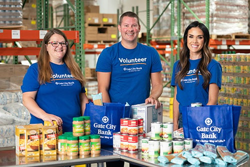 three Gate City Bank team members smile for camera while sorting donated food into the bank’s blue tote bags