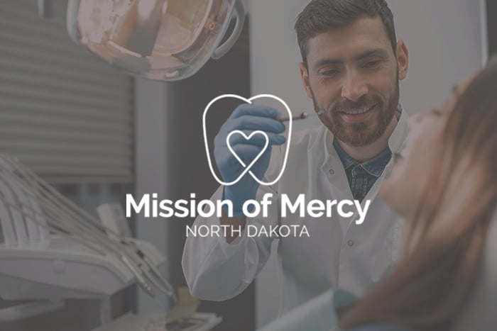 Mission of Mercy logo overlays an image of a friendly male dentist helping a patient
