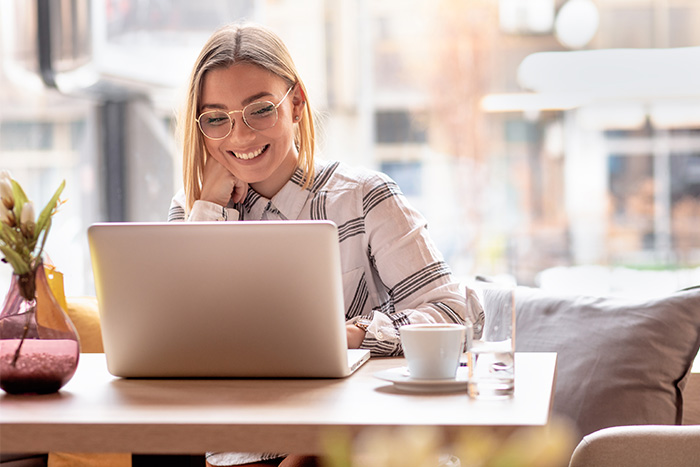 Twentysomething blonde woman with glasses, signing up for Gate City Bank mortgage rate alerts on her laptop at a coffee shop