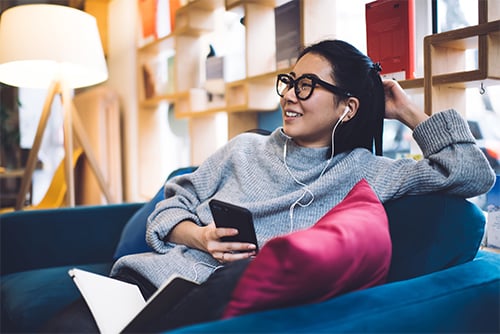 Relaxed Gen Z woman with earbuds and black rimmed glasses, applying for a debt consolidation loan on her phone in Fargo, ND