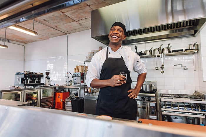happy chef holds water glass in his kitchen after securing helpful equipment loans