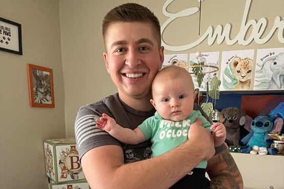 Bleau Hoge stands up and smiles for the camera while holding his baby daughter, Ember