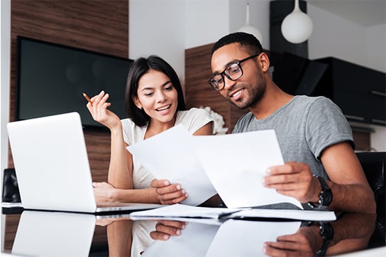 Young couple reviewing paperwork and trying out Gate City Bank's home equity loan calculator on their laptop