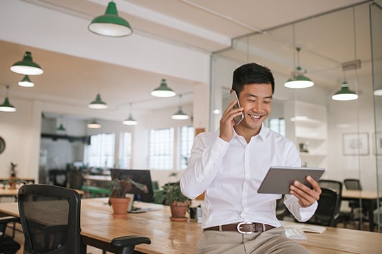 happy man in office enjoys money market savings with phone and tablet
