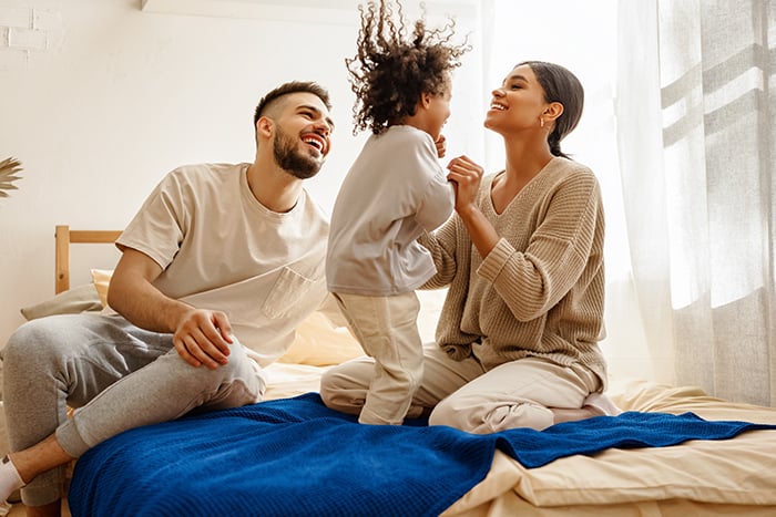 A father and mother laugh as their child jumps on the bed at their home in Fargo, ND.