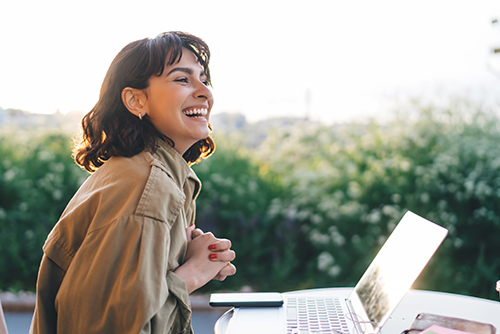 happy woman sits at patio table with laptop and scenic backdrop to read Gate City Bank’s article on keeping deposits secure with FDIC insurance