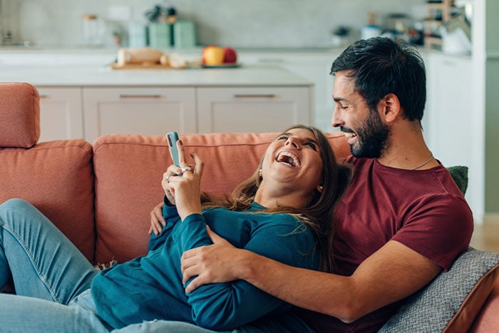 Married couple on the couch in their West Fargo home, applying via mobile for the North Dakota Primary Residence Credit