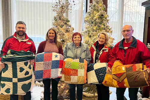 Gate City Bank team member Amy Durbin and four American Red Cross representatives line up and hold donated quilts inside the bank’s lobby in downtown Fargo North Dakota