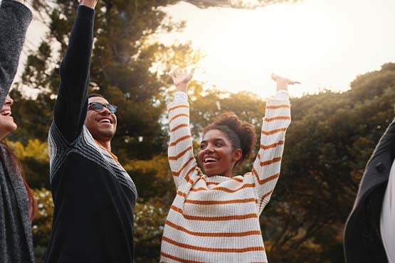 happy friends stand together on a bright sunny day and joyfully raise their arms up in the air in celebration