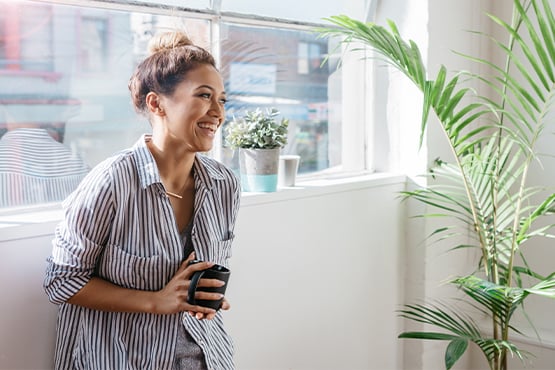 a young woman smiles and holds coffee after reading about Gate City Bank’s five budgeting tips for recent college graduates