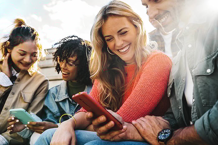 Group of young friends sitting on bleachers in sunny Fargo, ND, opening new Gate City Bank checking accounts via mobile