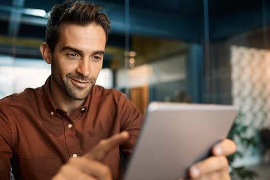 A smiling, confident male merchant prevents BIN attacks by checking for credit and debit card testing fraud with his tablet