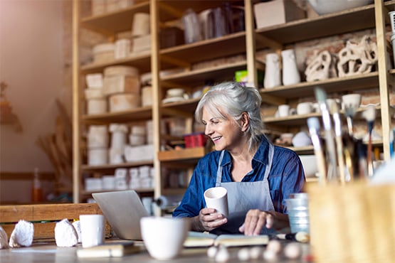 arts business owner holding a crafted cup and looking at her computer