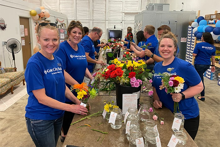 team members smile for the camera while they assemble bouquets for Hope Blooms