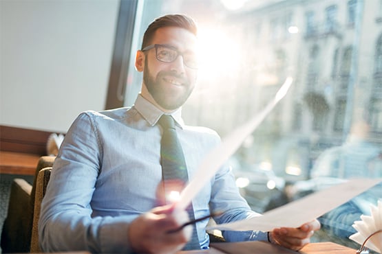 male lender with glasses dress shirt and tie looks through papers at desk