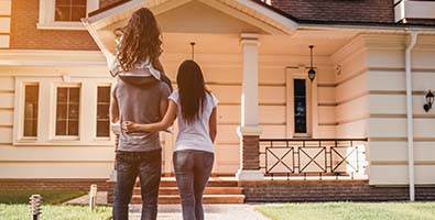 wife and husband with daughter on his shoulders gaze upon their dream home after securing a mortgage loan in Fargo, ND