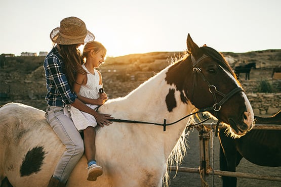 Mom and her young daughter riding bareback together on a paint horse at sunset on the edge of Hettinger, ND