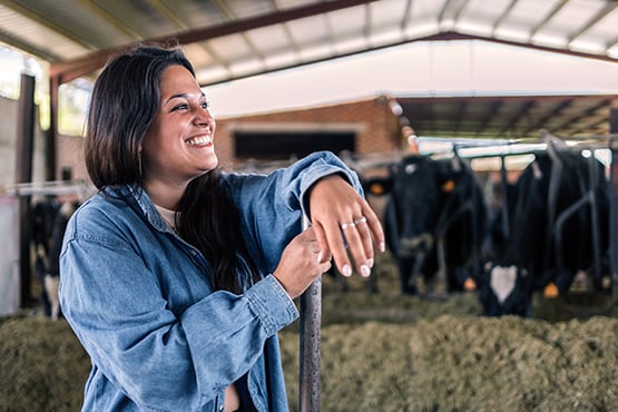 Smiling farmer with her arm resting on a pitchfork, standing in front of a row of Holstein dairy cattle near Jamestown, ND
