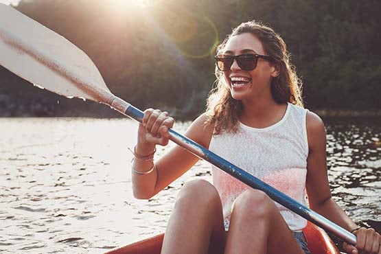 Laughing brunette in sunglasses, paddling her kayak across Pebble Lake in Fergus Falls, Minnesota