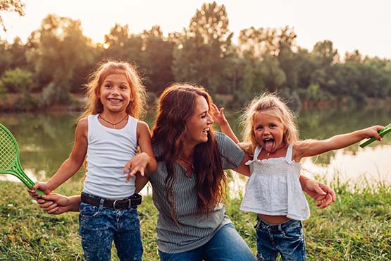 Laughing mom with her two young blond daughters, playing badminton on a summer day in Park River, ND