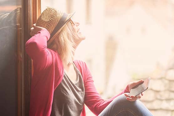 Joyful blonde woman with fedora sunglasses and phone enjoys premium interest checking outside