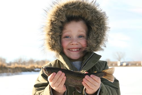 happy boy in parka holding up his prize catch while ice fishing