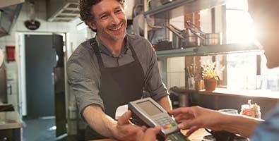 smiling business owner in apron holds a pos system for happy customer to make purchase after receiving loan from gate city bank