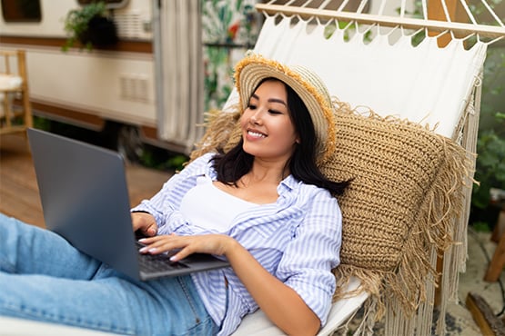 woman in a sunhat relaxing in her hammock while trying out Gate City Bank’s personal loan calculator on her laptop 