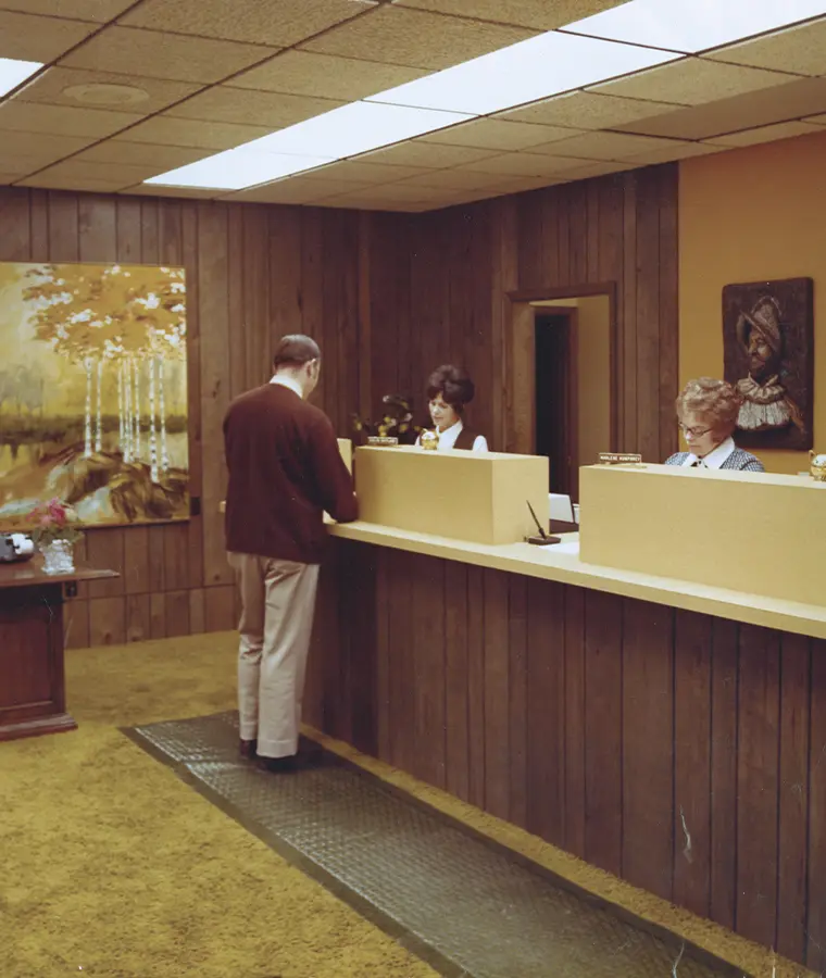 1970s color photo of two Gate City Bank female tellers assisting a male customer in the lobby