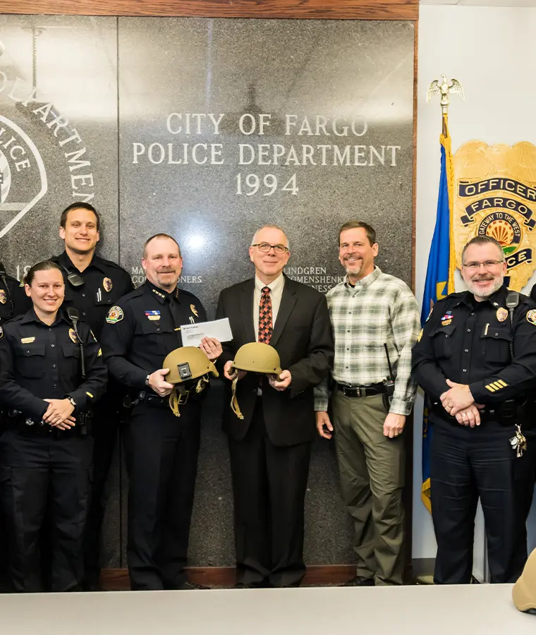 1990s color photo of former president and CEO Steve Swiontek posing with Fargo police officers after donating protective helmets