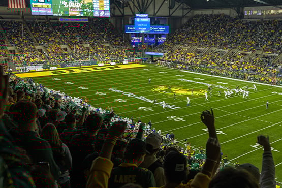 A crowded stadium at Gate City Bank Field during an NDSU Bison football game, with fans cheering and hands in the air