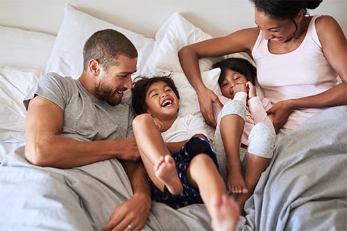 family of four laughing in bed on a Sunday morning in their new home in Fargo, ND, built with a Gate City Bank construction loan